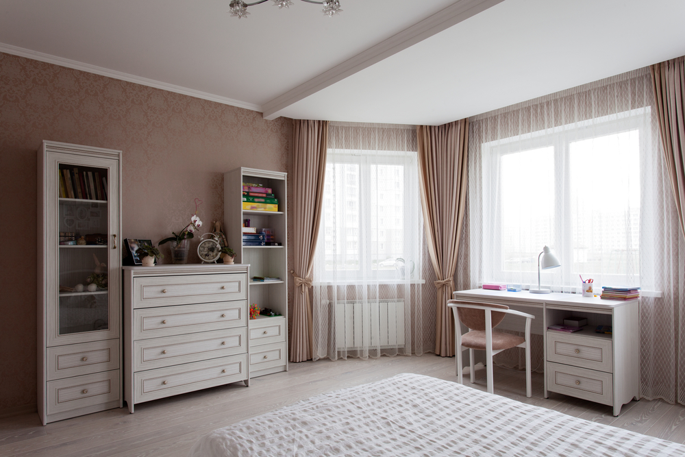 White chest of drawers, bad and a writing desk near the window in a room